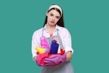 Young tired housewife wearing casual clothes, latex gloves holding full basin of cleaning agent, isolated backgroundの写真素材
