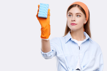 Housemaid wearing orange rubber gloves for hands protection washing with sponge. Cleaning or...