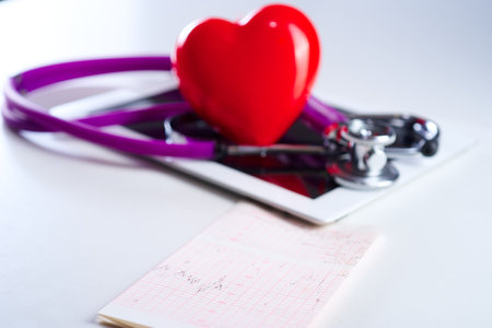 Medical stethoscope and a red heart and tablet with cardiogram on white background. Technology concepts and treatment of heart disease.の写真素材