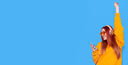 Smiling girl listen music on headphones and holding smartphone on blue backgroundの写真素材