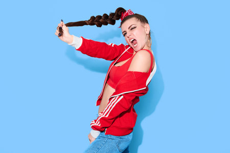 Young hipster teenage girl in bright casual retro clothes and long hair have fun on blue background