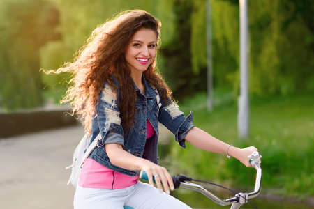 European girl with beautiful smile rides bicycle in the city in the summer. Woman in casual clothes...
