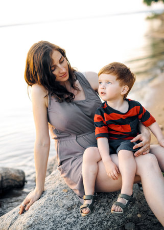 Young happy pregnant mom plays with her young son on the lake in summer.の写真素材
