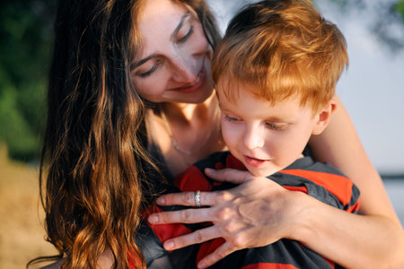 Young happy smiling mother holds her young son in her arms and smiles. The relationship of mom and sonの写真素材