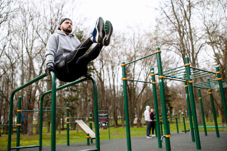 Young strong man doing ABS exercises on the uneven bars on the sports field in the summer in the...