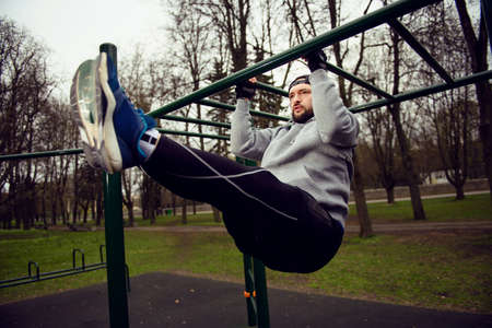 Young strong man abs exercises on a horizontal bar on a sports ground in the summer in the cityの写真素材
