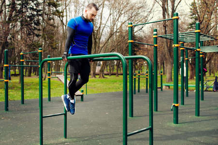 Young strong man doing the exercises on the uneven bars on the sports field in the summer in the cityの写真素材