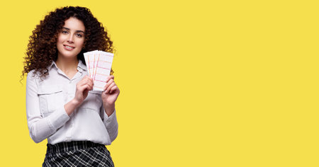 Excited young curly girl holding lottery tickets isolated over yellow backgroundの写真素材