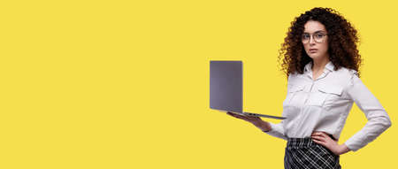Curly girl in glasses and white shirt holding laptop computer isolated over yellow backgroundの写真素材