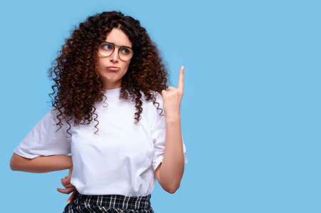 Upset curly hair woman pointing finger up on blue backgroundの写真素材