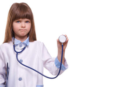 Medical concept. Cute serious little girl doctor wearing white coat holds stethoscope on white isolated backgroundの写真素材