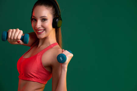 Fitness woman with strong body doing exercise with dumbbells indoors and listen music in headphonesの写真素材