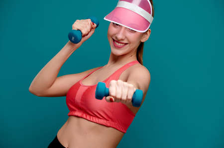 Smiling attractive caucasian sporty woman with athletic strong body do exercise with dumbbells indoorsの写真素材