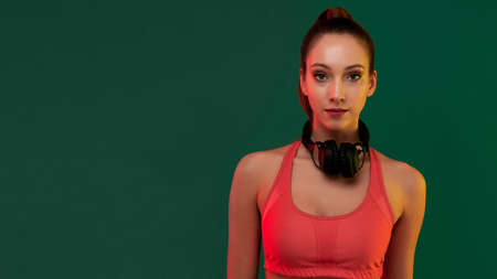 Young smiling sportive girl listening to music on headphones after playing sports exercise