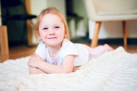Cute little girl lying on the floor at home and smileの写真素材