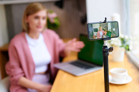 Selective focus of woman blogger broadcasts live on phone at home next to laptop
