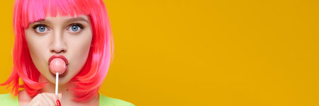 banner format. Freaky hipster woman in pink wig eat lick lollipop on bright yellow backgroundの写真素材