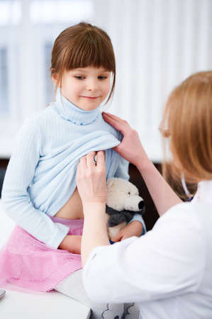 Cheerful female doctor checking patient little girl by stethoscope in hospitalの写真素材