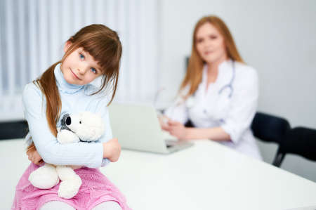 Little girl patient with doctor holds toy bear and smile in hospitalの写真素材