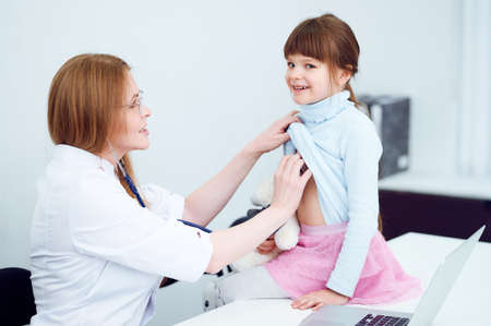 Caucasian female doctor examining patient little girl by stethoscope in officeの写真素材