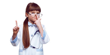 Happy cute little caucasian preschooler girl in white medical uniform and glasses act like doctor, portrait of smiling small child in whites have fun playing in hospital, career concept.の写真素材