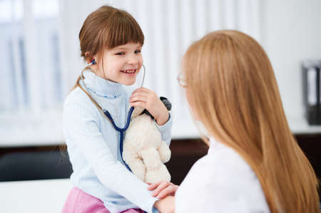 Little girl patient checking heartbeats female doctor in hospital by stethoscopeの写真素材