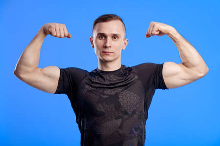 Strong muscular bodybuilder guy demonstrates his muscles isolated on a light blue background....