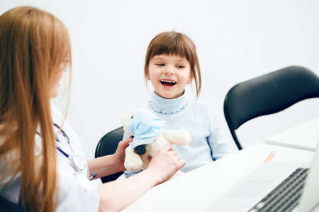 Female caucasian doctor with little girl patient and teddy bear toy in office hospitalの写真素材