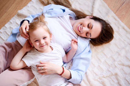 Happy single mother with her daughter is lying on the floor and smiling. The relationship between parents and childrenの写真素材