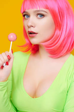 Seductive woman on pink wig eat or lick big lollipop on bright yellow backgroundの写真素材