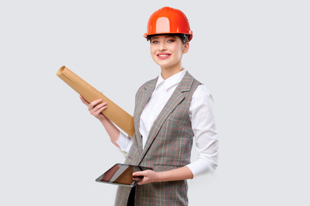 Caicasian young female engineer in helmet and goggles holding blueprints isolated on whiteの写真素材