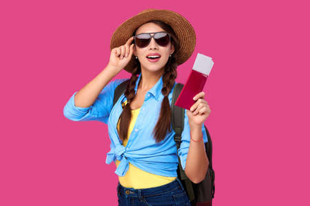 Woman tourist with traveling tickets and passport over pink isolated background. Female traveler in summer straw hat and sunglasses over pink isolated background. Tourism conceptの写真素材