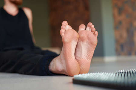 Mans feet after standing on sadhu board (yoga board). Male sitting on the floor in yoga studio after practice indoorsの写真素材