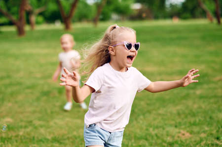 Little girl in sunglasses is running around the summer park and having fun with her sister. Family vacation in the city. Happy childhoodの写真素材