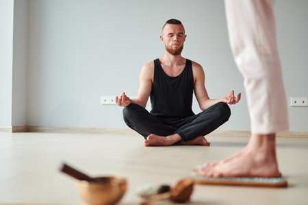 Woman legs standing on wooden yoga Sadhu Board with nails for practice and meditation and man meditation on lotus position. Alternative medicine acupressure, recovery strengthの写真素材