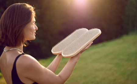 Caucasian woman holds sadhu nail board outdoors. Concentrated female practicing yoga alone on the grassの写真素材