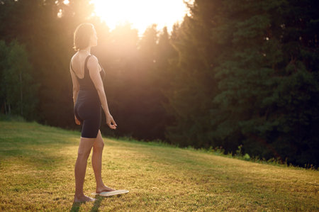 Meditate caucasian woman standing on Sadhu nail board with closed eyes during concentration meditation practice on summer field. Concentrated female practicing yoga alone outdoors.の写真素材