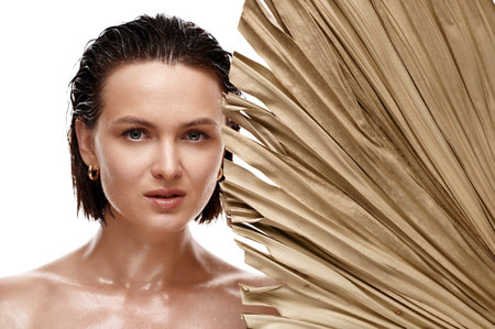 Organic beauty shot of an attractive woman with hydrated skin and wet hair holding a dry palm leaf, emphasizing the importance of skincare and eco-friendly beautyの写真素材