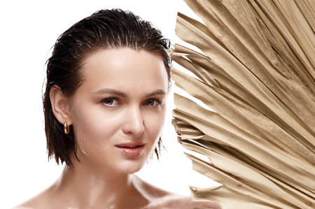 Beauty shot of an alluring woman with wet skin and hair holding a dry palm leaf, emphasizing natural skincare and organic beautyの写真素材