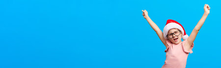 Happy new year concept. Happy screaming caucasian girl wearing glasses and santa claus red hat shows thumb up on blue isolated background. Banner formatの写真素材
