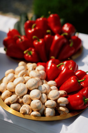 White mushrooms and red bell peppers arranged on a golden plate, placed on a white surfaceの写真素材