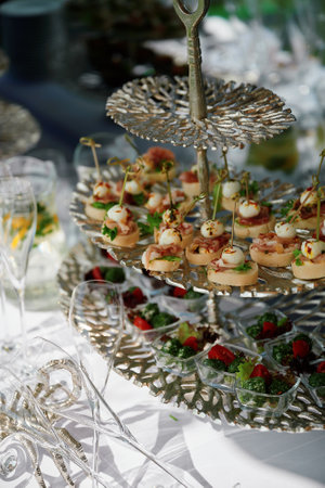 Tiered serving tray with cheese canapÃ©s garnished with herbs and bacon bits on the top tier, and leafy salad with cherry tomatoes in clear cups on the lower tier, surrounded by champagne flutesの写真素材