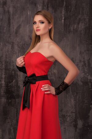 Beautiful young woman in red dress posing on the grey background. Fashion photo.の写真素材