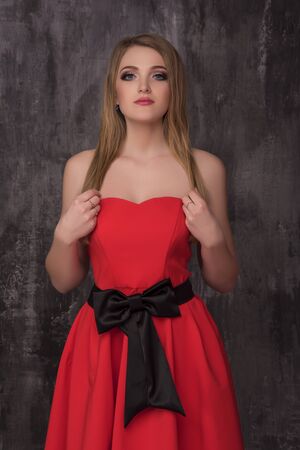 Beautiful young woman in red dress posing on the grey background. Fashion photo.の写真素材