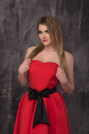 Beautiful young woman in red dress posing on the grey background. Fashion photo.の写真素材