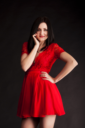 Portrait of  smiling young brunette woman in red dress on the black backgroundの写真素材