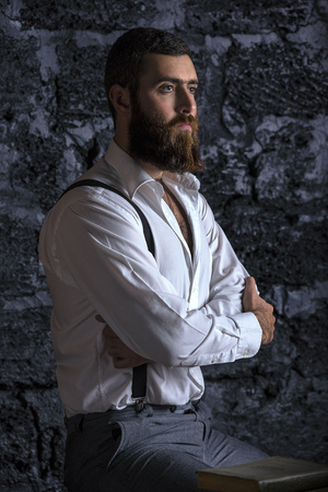 Serious and brutal businessman in thinking process. Dark hair and beard wearing jacket. Against the wall.の写真素材