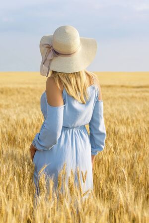 Travel tourism. Woman at sunset in yellow wheat in blue dress and hatの写真素材
