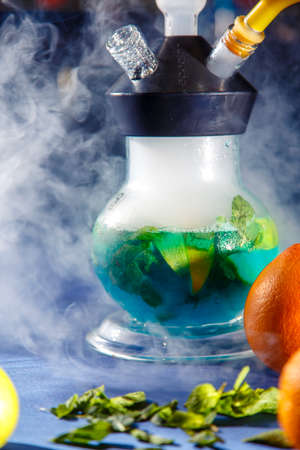 round hookah flask with green liquor. Sliced grapefruit and mint leaves float in the liquor. Lots of...