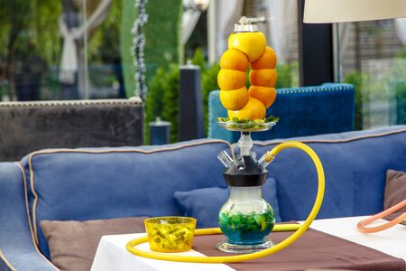 Hookah on the orange. Orange hookah. Hookah with a round transparent flask in which sliced oranges and mint leaves float in red liquor. The hookah bowl is made of several oranges connected to each other. Lots of smoke. Black backgroundの写真素材
